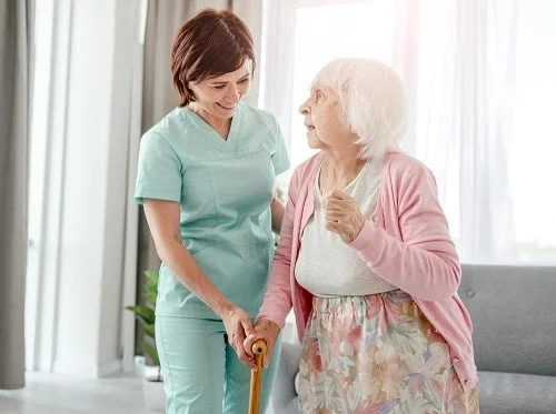 A carer helping an older woman walk with her stick
