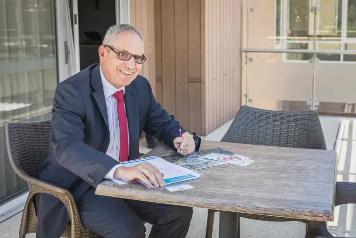 Lewis Chiat at an outdoor table with paperwork, smiling