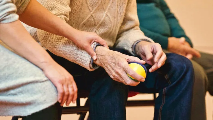A carer resting a hand on an older person's hand as they hold an exercise ball